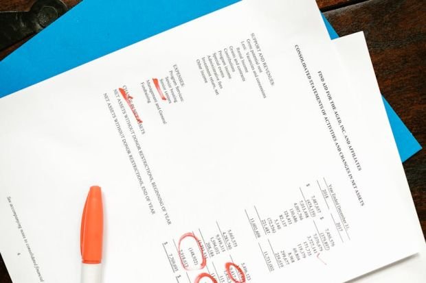 Overhead view of financial documents with red highlighted sections on a wooden desk.