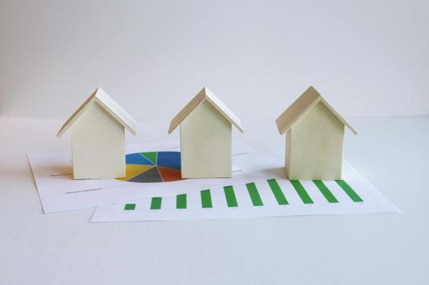 Wooden model houses on graphs depict real estate market analysis and trends.