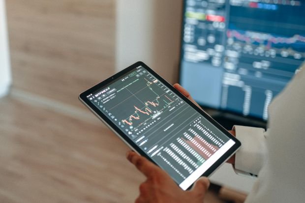 A person uses a tablet to monitor stock market trends and real-time trading graphs.