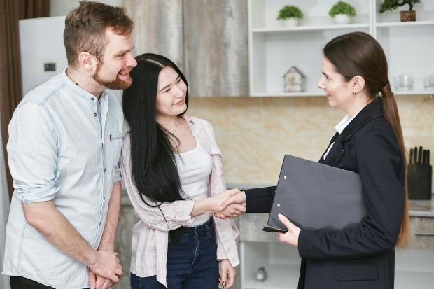 A real estate agent greets a couple with a handshake in a modern home interior.