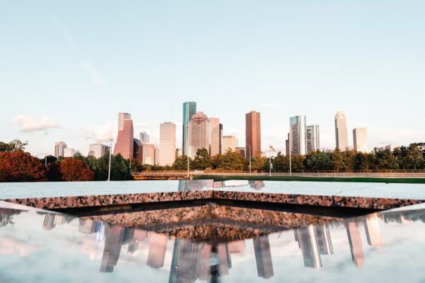 Stunning skyline of Houston with city buildings reflecting on a water surface, under a clear sky.