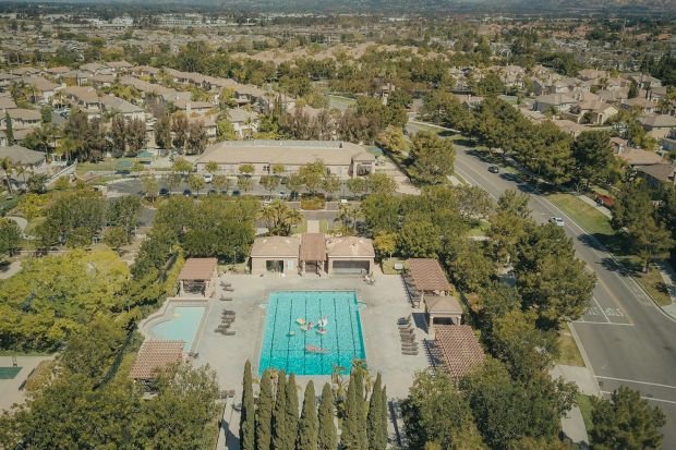 Aerial view of a residential neighborhood with a busy swimming pool and surrounding greenery.